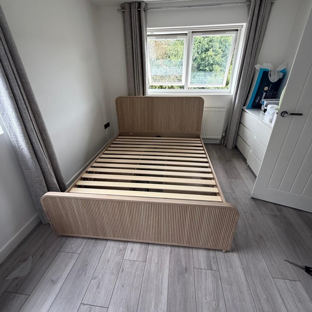 Oak slatted bed frame assembled in a bedroom with grey laminate flooring