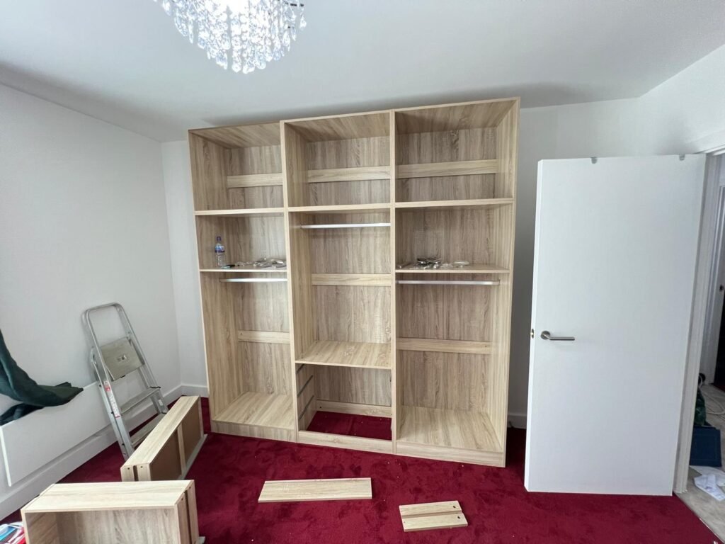 Flat-pack wardrobe carcasses built and lined up against a bedroom wall, doors still to fit