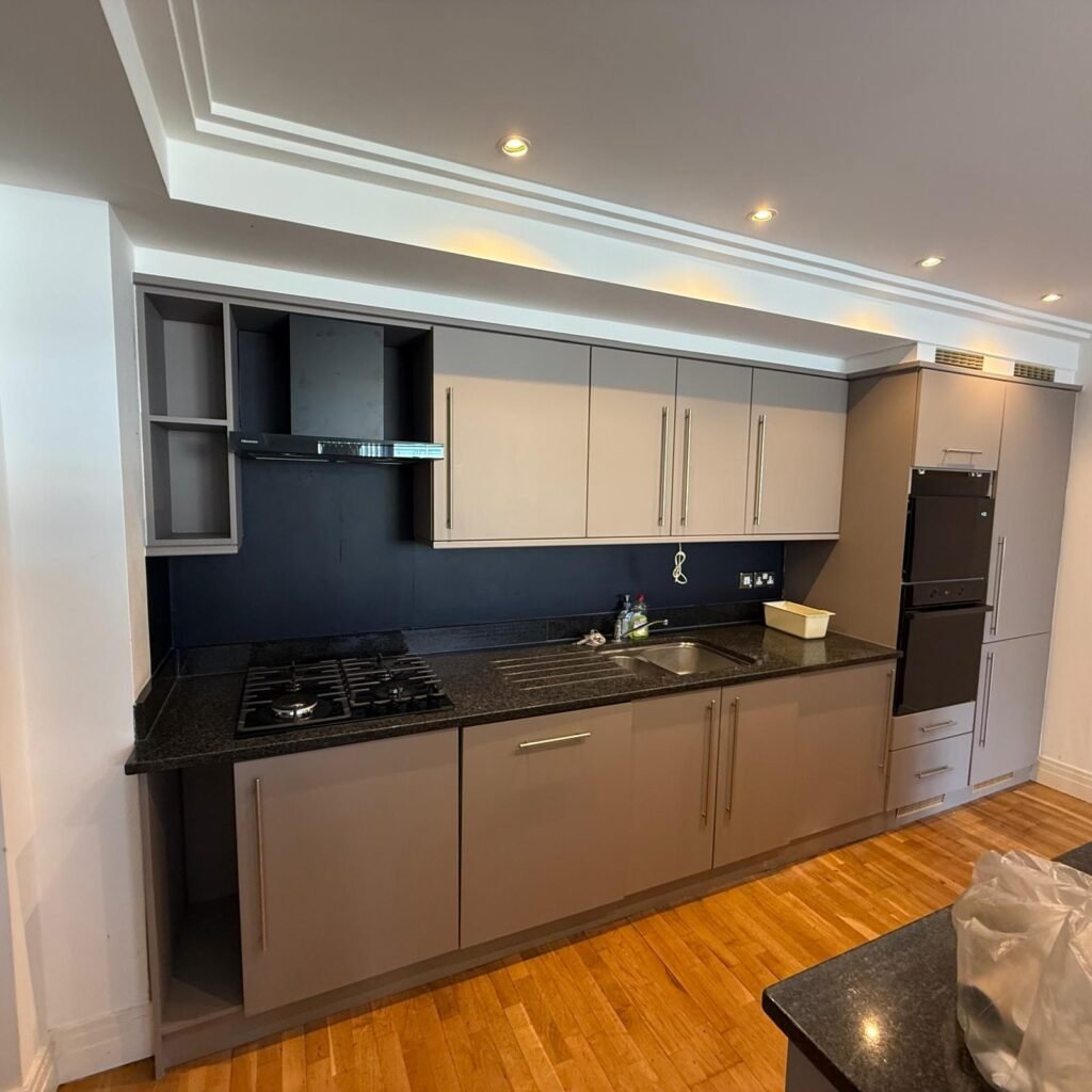 The same kitchen after refurbishment with taupe doors, black splashback and new appliances