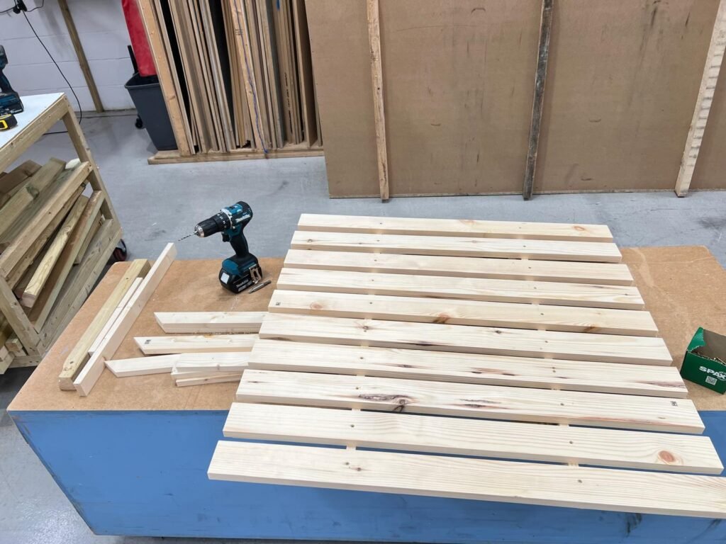 Pine slatted shelves being built on a workshop bench with a drill and screws
