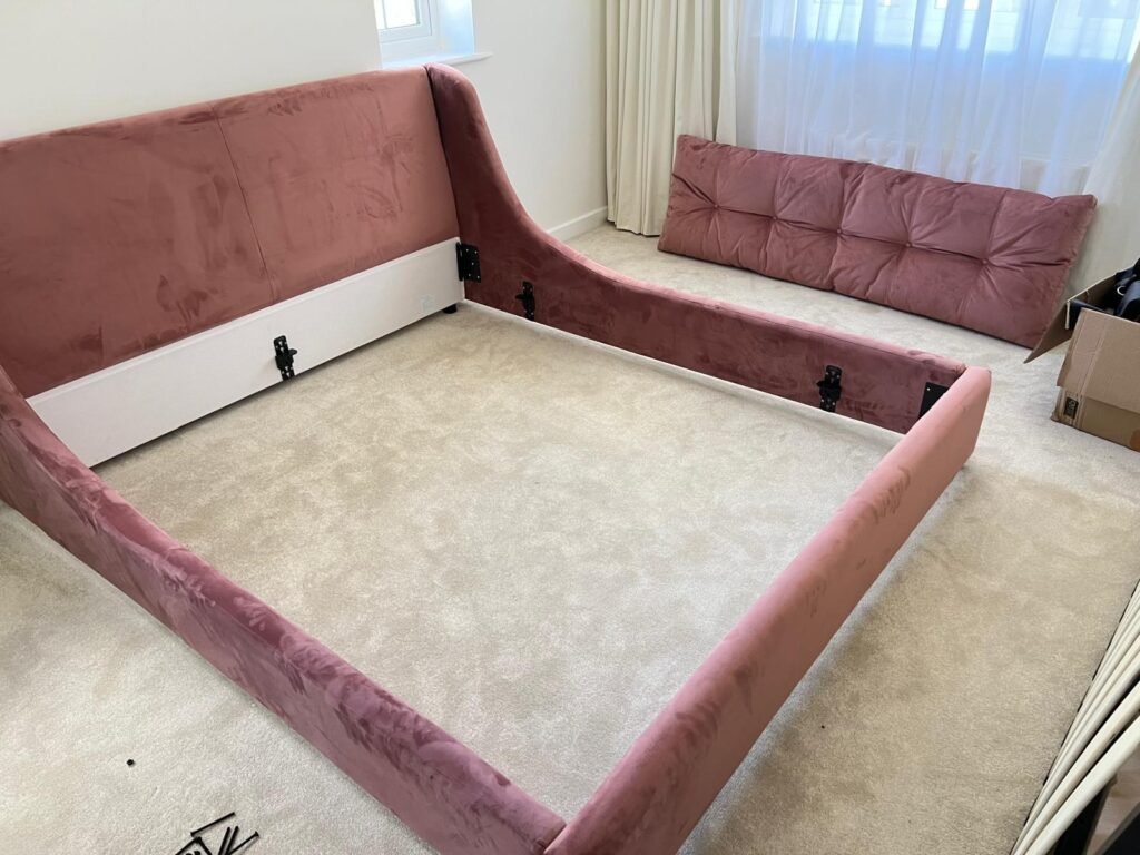 Upholstered pink velvet bed frame being assembled in a bedroom